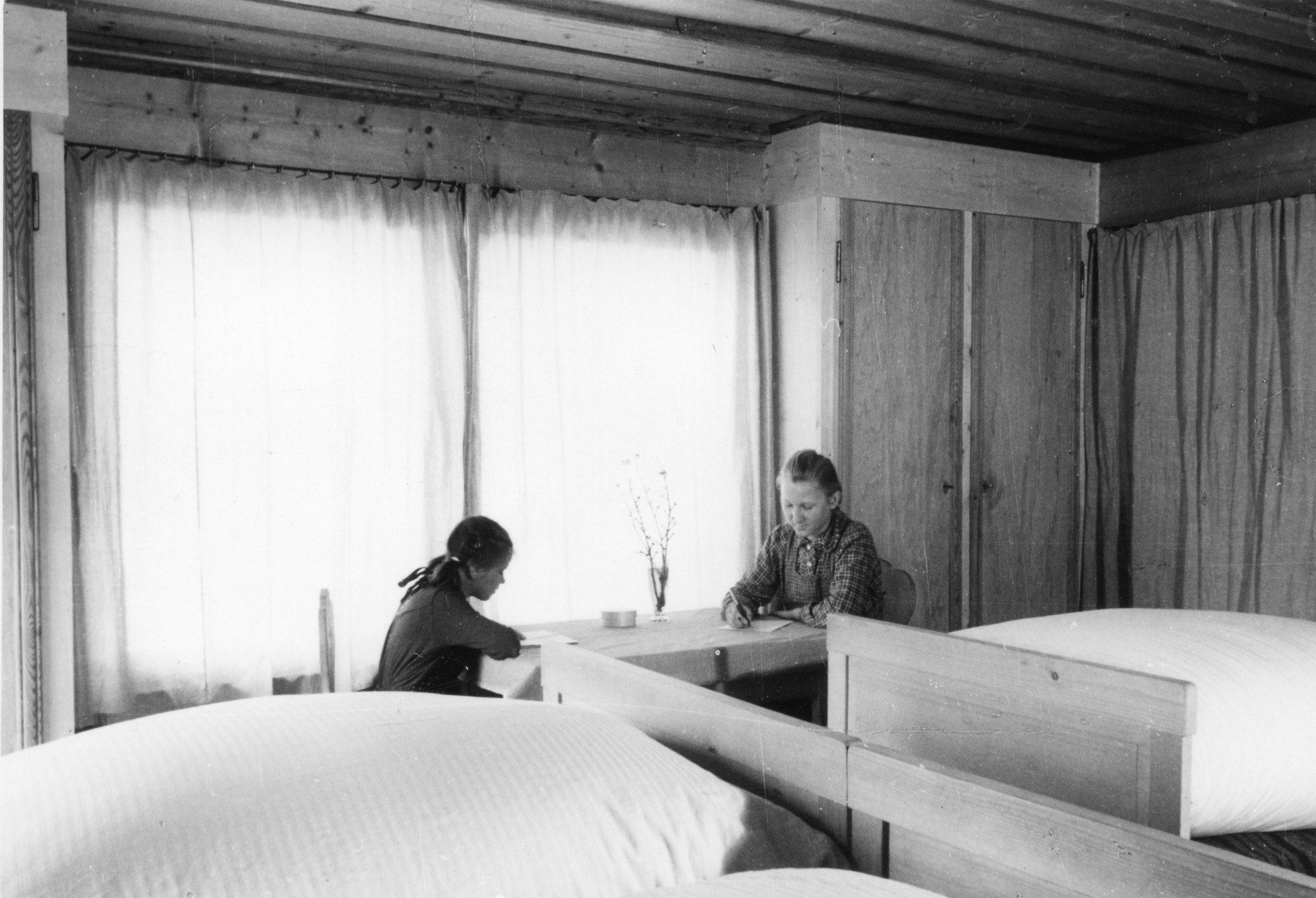 Zwei junge Frauen lesend und Briefe schreibend in einem Schlafzimmer sitzend, vermutlich ein Kinderheim