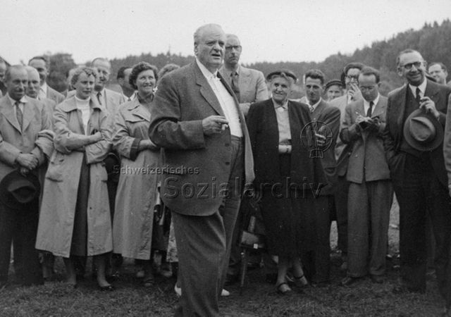 Männer und Frauen bei einer Veranstaltung, ein Mann hält eine Ansprache; um 1960