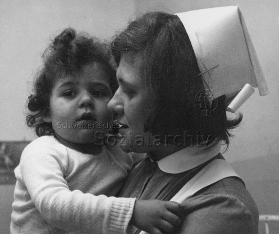 "Heimkinder" - Betreuerin hält kleines Kind im Arm; um 1960