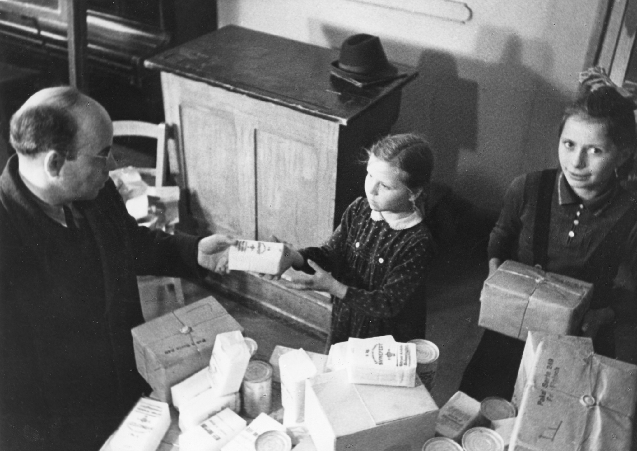 "März 1948: Verteilung von Lebensmittelpaketen am die Schüler der Gemeinschaftsschule Düsseldorf"; ein Mädchen von einem Mann eine Packung entgegennehmend