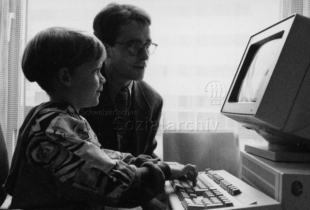 Kinder besuchen ihre Eltern am Arbeitsplatz - Sohn sitzt im Büro des Vaters am Computer; um 1995