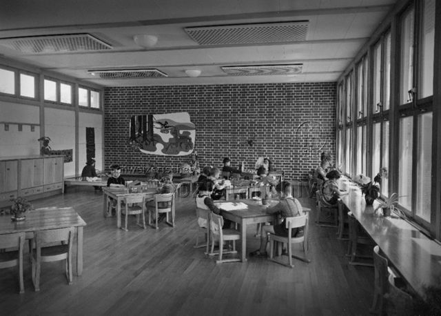 "3 Kindergärten, Burgfelderstrasse, Basel, Arch. Hochbauamt" - Kinder sitzen an Tischen und spielen oder lesen; um 1960