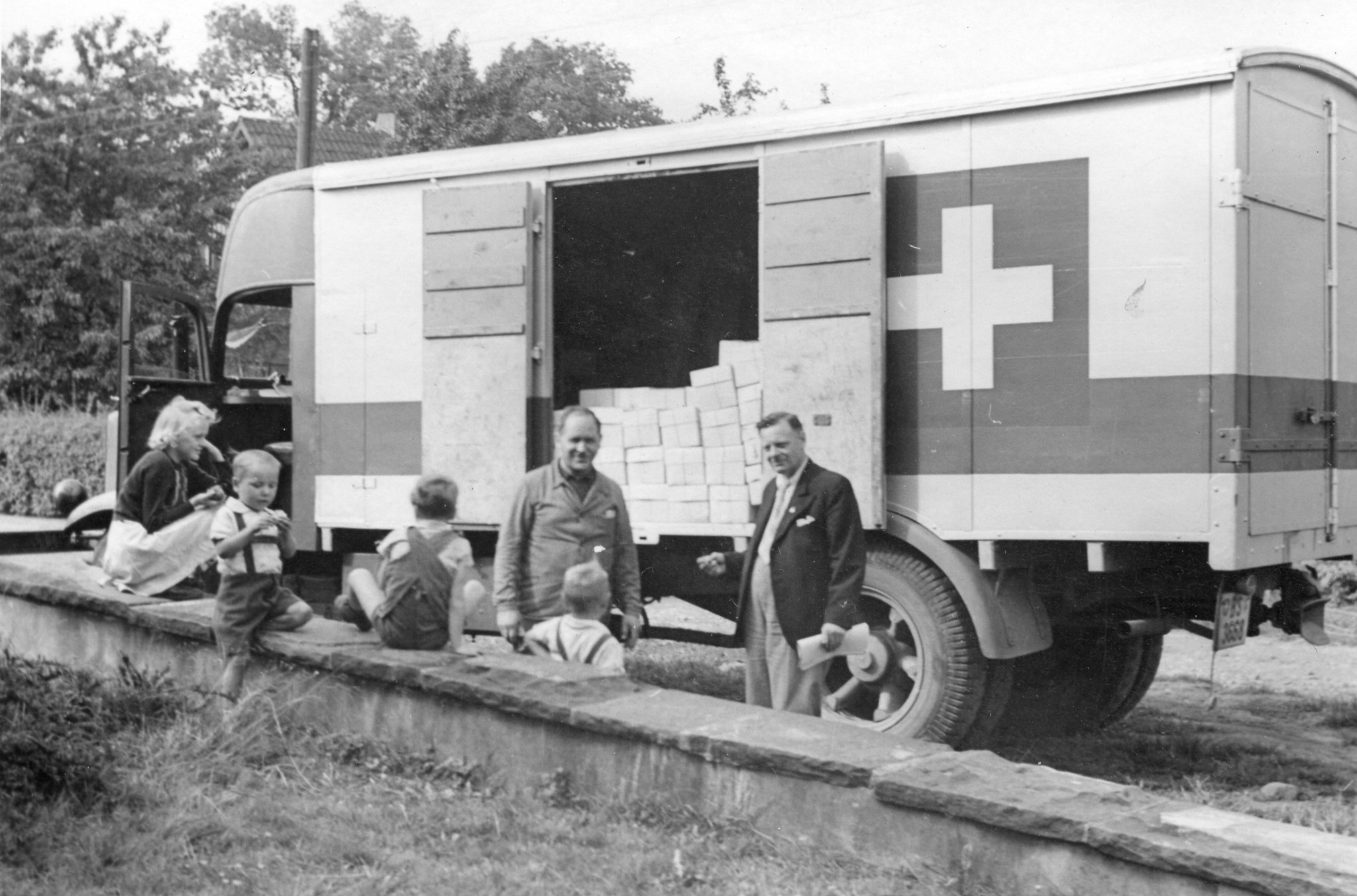 "Der Schweizerwagen auf seiner Tour in Deutschland 1946"; Männer und Kinder stehen vor einem Transporter mit der Schweizer Flagge