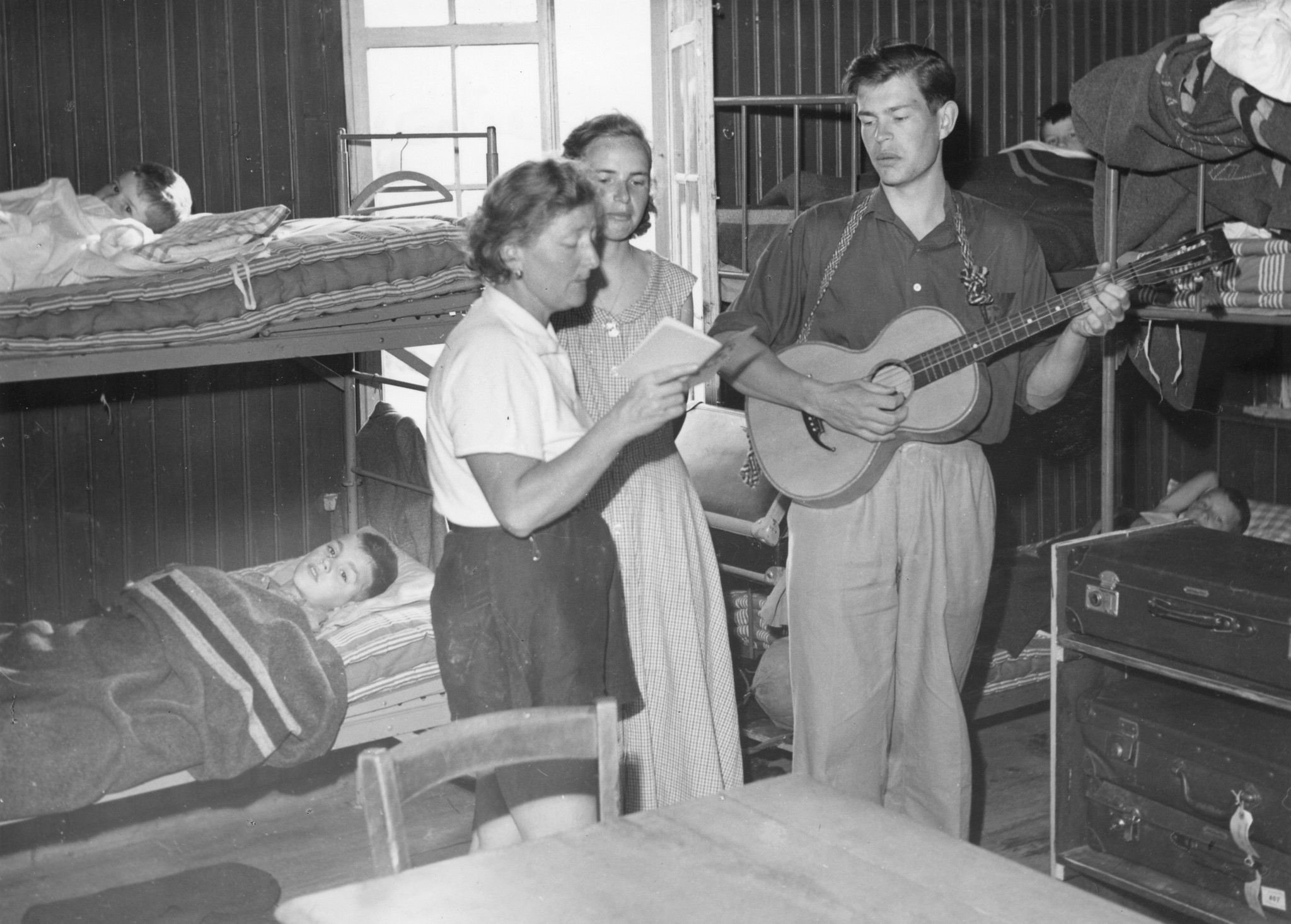 Ferienkolonie Landmark: Drei Betreuer singen in Gitarrenbegleitung ein Lied für die Kindern, die in den Betten liegen