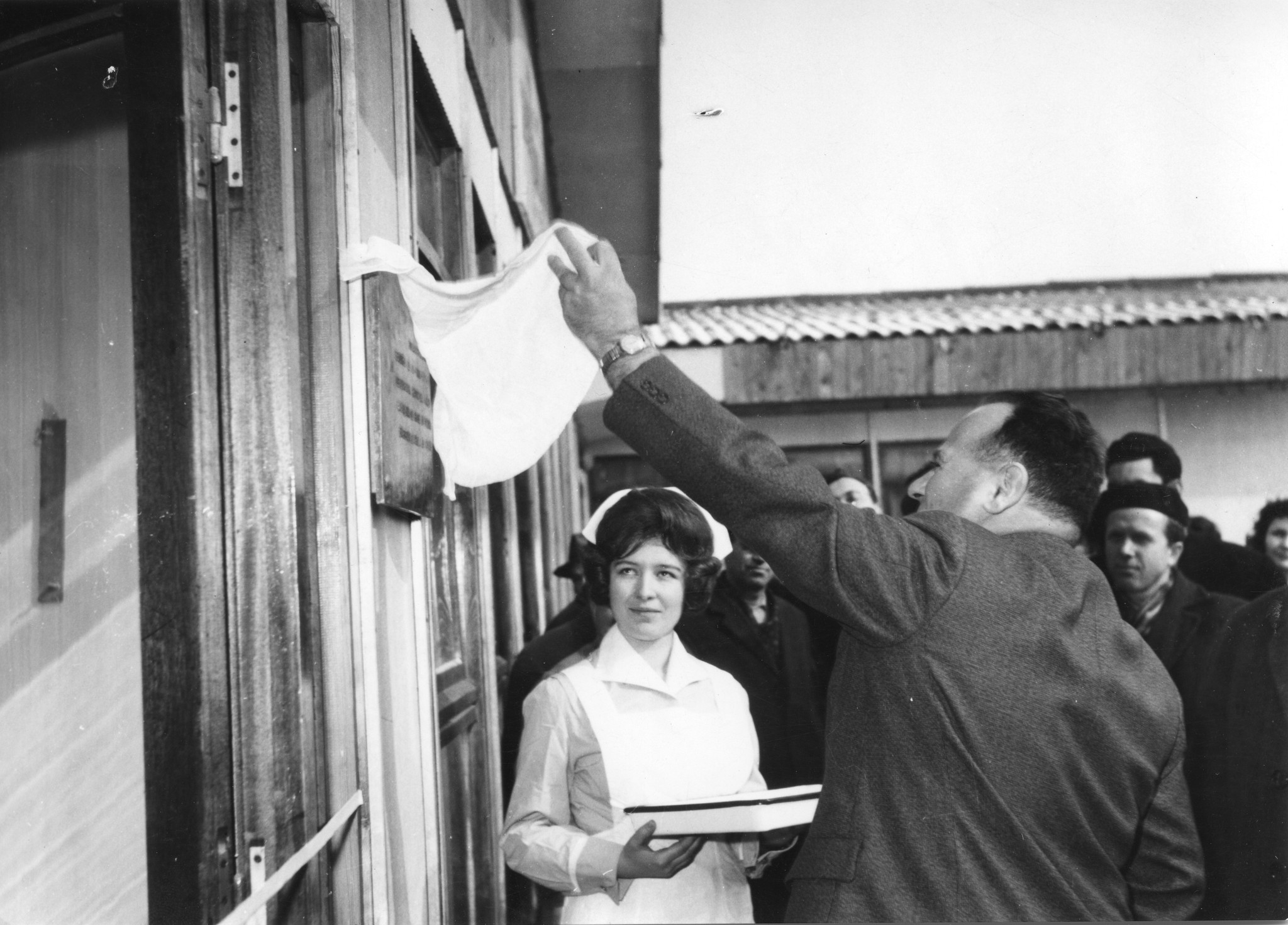 Röbi Risler enthüllt mit einem weissen Tuch die Beschriftung des neuen Ambulatoriums, Skopje, 1965