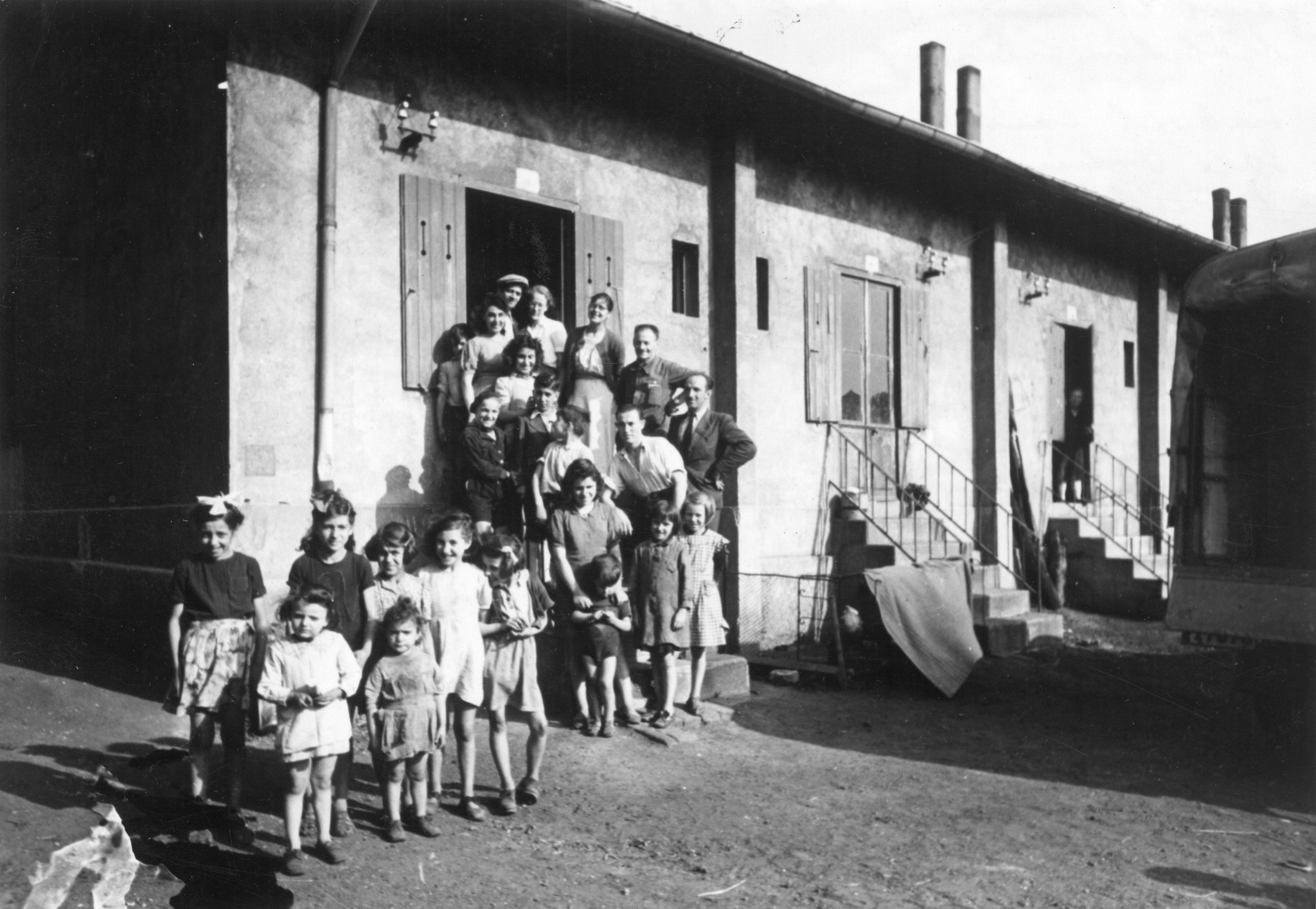 "Saint-Etienne, 7. Juli 1945. Möbelverteilung. Fabrikhäuser "Cité du Marais". Jede Wohnung besteht aus 2 Zimmern. 1 Türe vorne, 1 Fenster nach hinten sind die einzigen Licht- und Luftspender. Ca. 20 Wohnungen sind aneinandergebaut." Hausbewohner