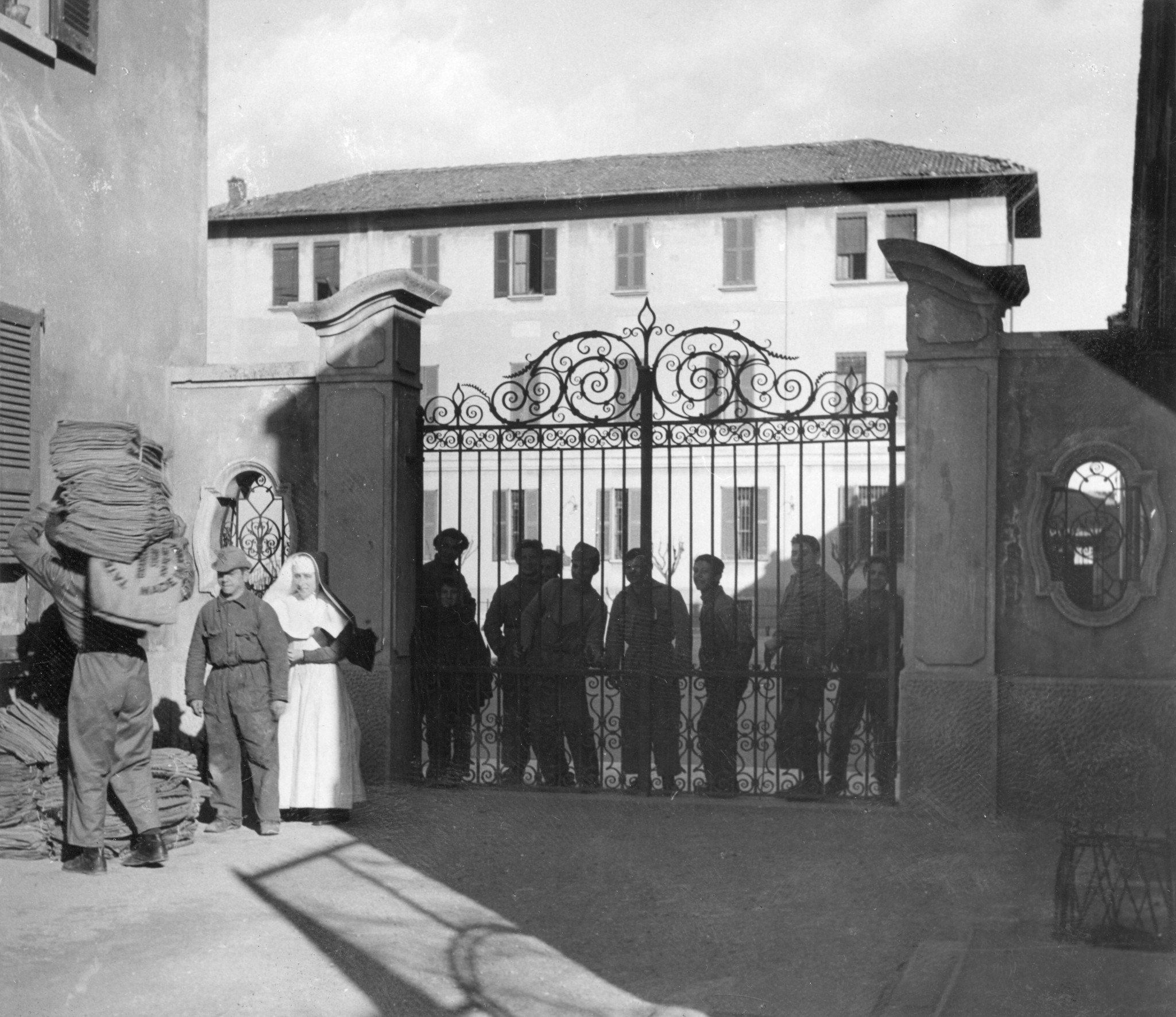 "Schwererziehbarenheim "Cesare Beccaria" in Arese bei Milano / Prätuberkulosenheim in Sovere", "Journalistenreise der Schweizer Europahilfe Febr.1949", Insassen schauen nach draussen beim Tor, eine Schwester, Arbeiter tragen Jutesäcke