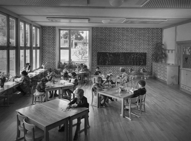 "3 Kindergärten, Burgfelderstrasse, Basel, Arch. Hochbauamt" - Kinder sitzen an Tischen und spielen oder lesen; um 1960