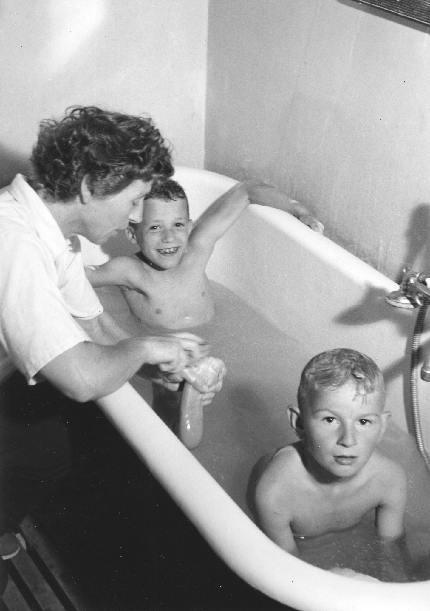Eine Frau badet zwei Jungen in der Badewanne