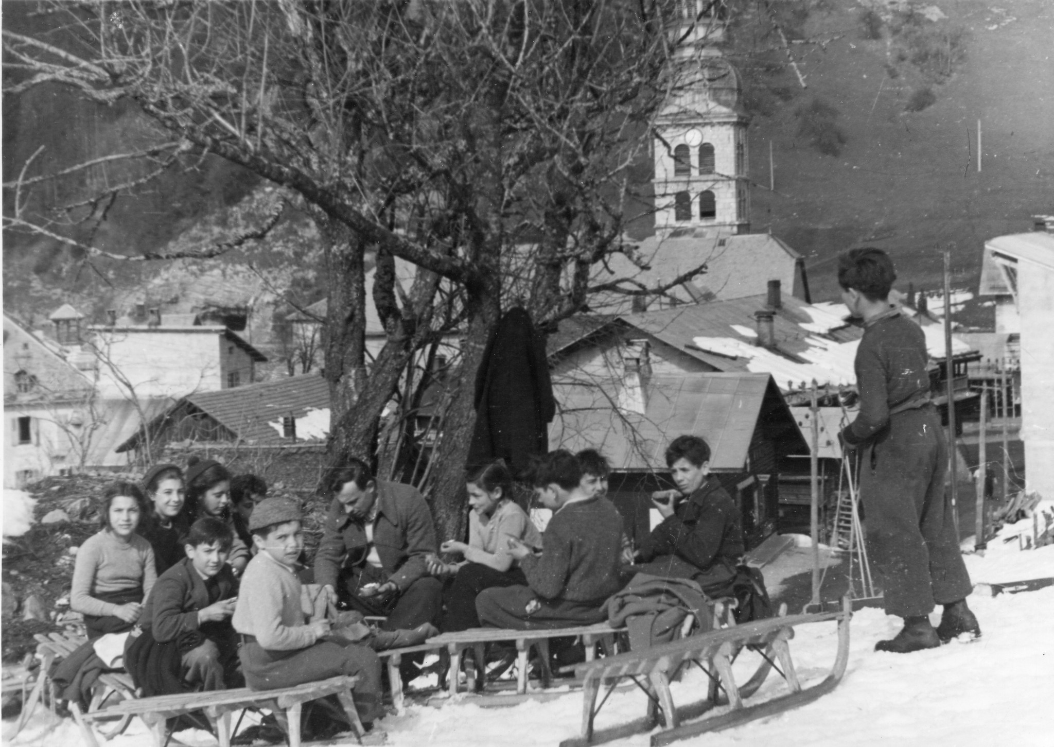Kinder und Betreuer sitzen auf ihren Schlitten, im Hintergrund ein Kirchturm