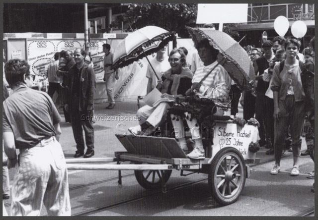 Stonewall-Demo (1989, Zürich) – Anhänger mit Aufschrift: "Sillberne Hochzeit - ♀♀ 25 Jahre [...]", darauf zwei Frauen mit Sonnenschirmen