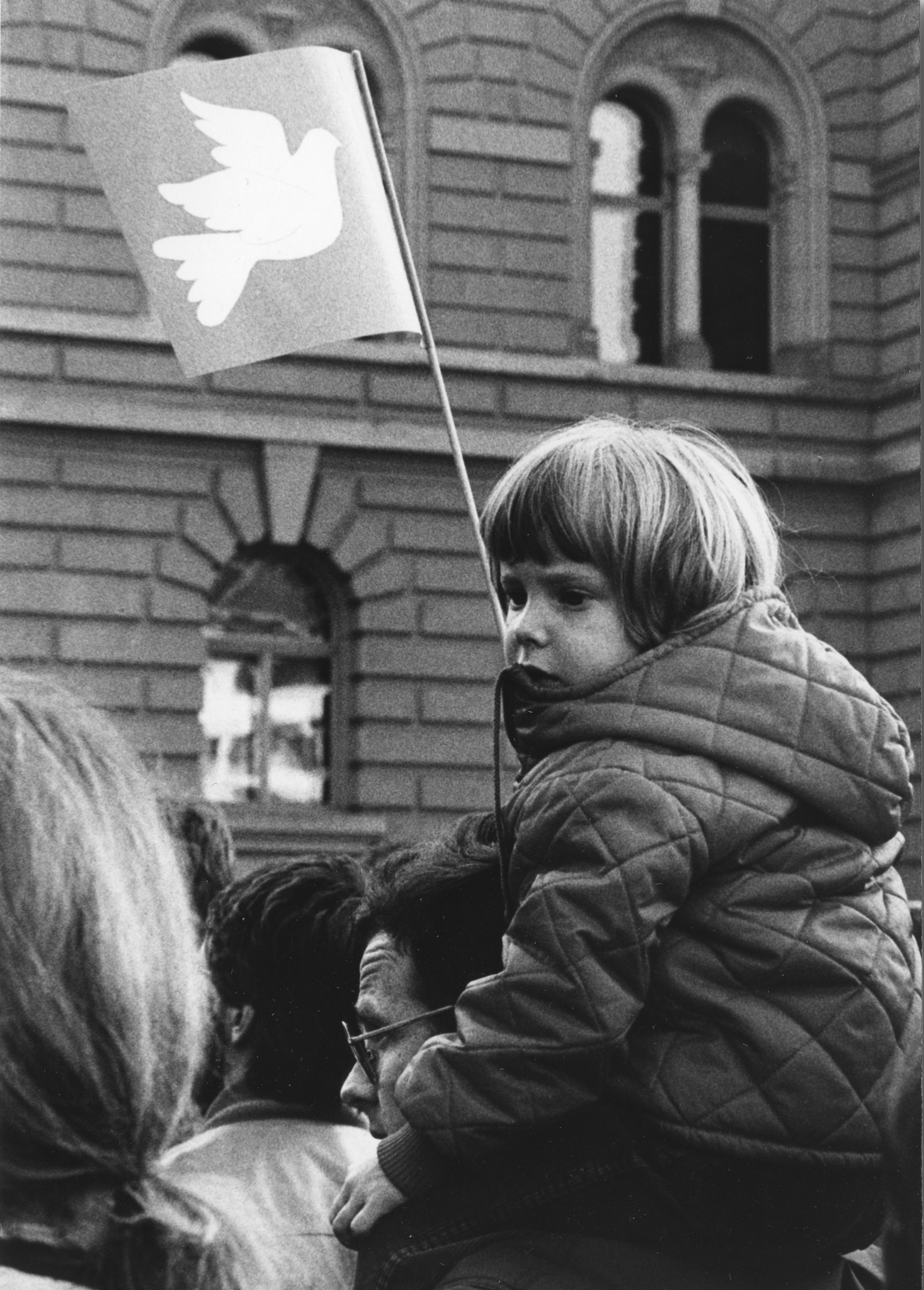 Ein Kleinkind mit einer Fahne der Friedenstaube auf den Schultern eines Mannes sitzend; von der SAH organisierte Friedensdemonstration im November 1983