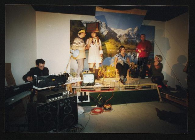 Performance, Gruppe GMAM (München/Berlin), auf Podest vor Tapete mit Alpenpanorama