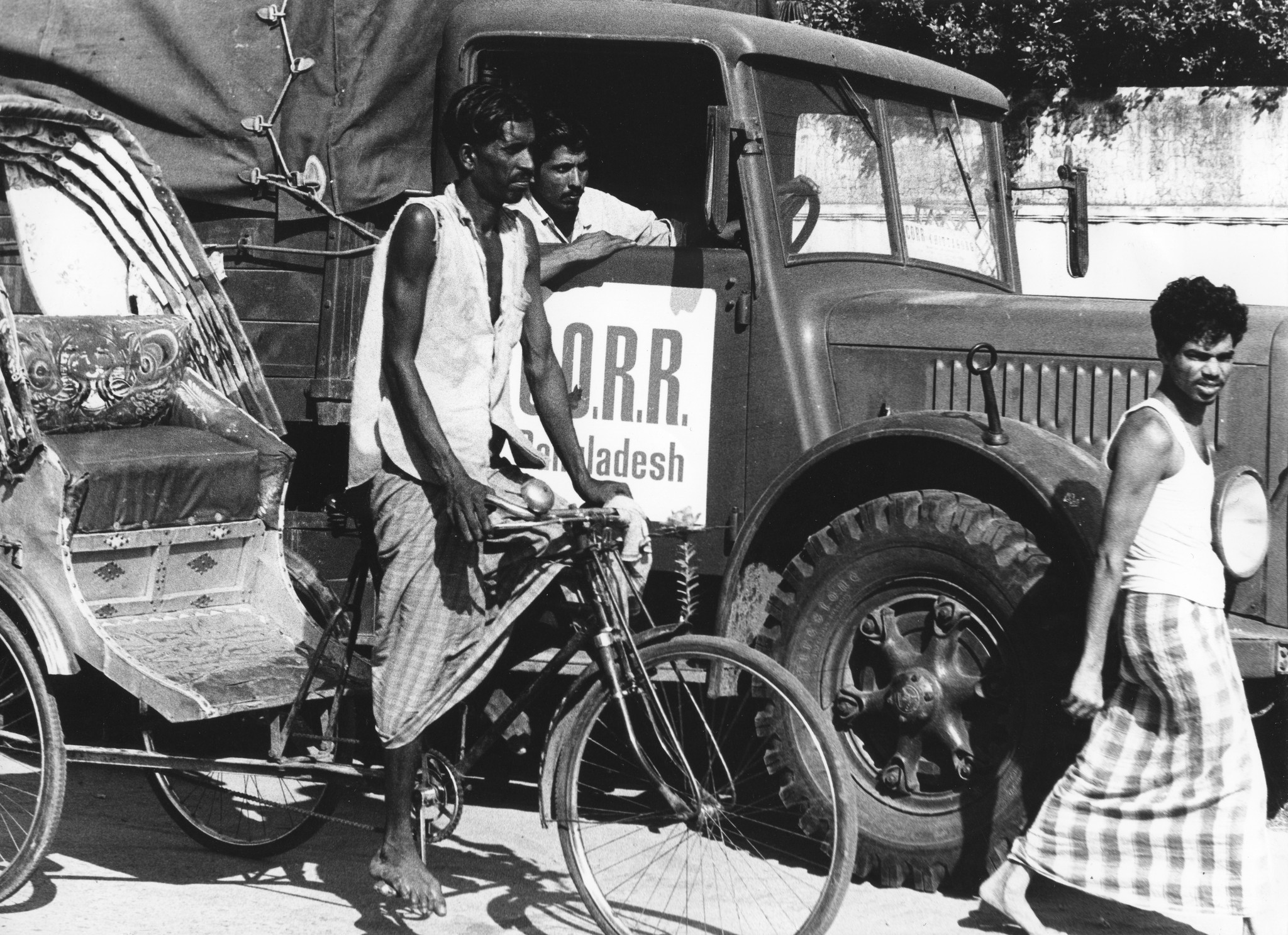 "Bangladesh: Swiss Truck Team Oktober 1972"; ein Einheimischer auf einer Rikscha neben einem Hilfsgüterlastwagen herfahrend