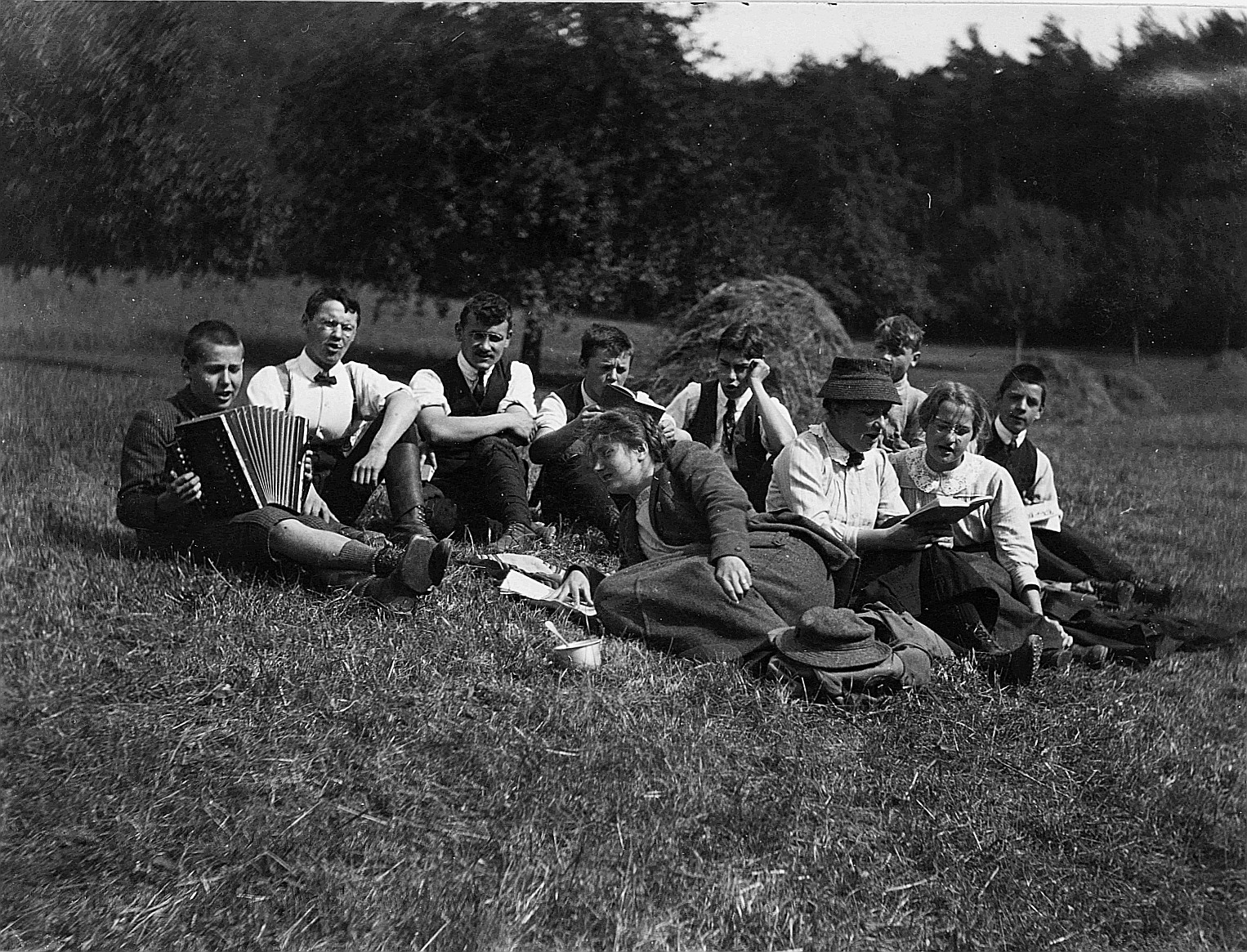 Singende Wandervögel sitzen auf der Wiese, ein Wandervogel Akkordeon spielend (1912)