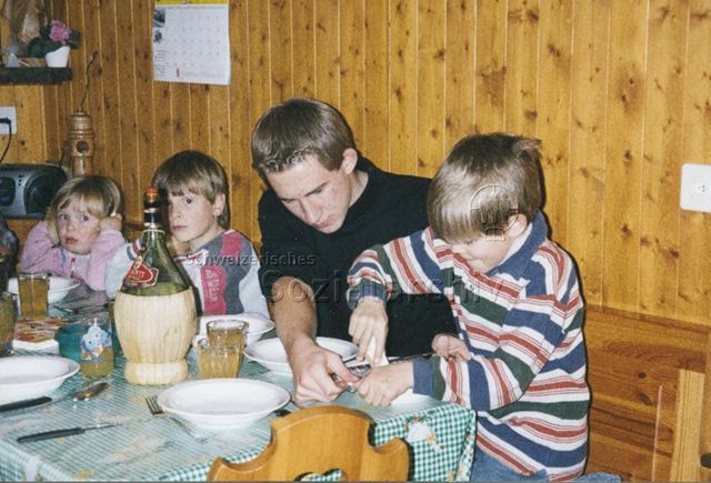 PraktikantInnenhilfe: Einsätze - Praktikant sitzt mit Kindern am Tisch und hilft beim Käsereiben; 2000