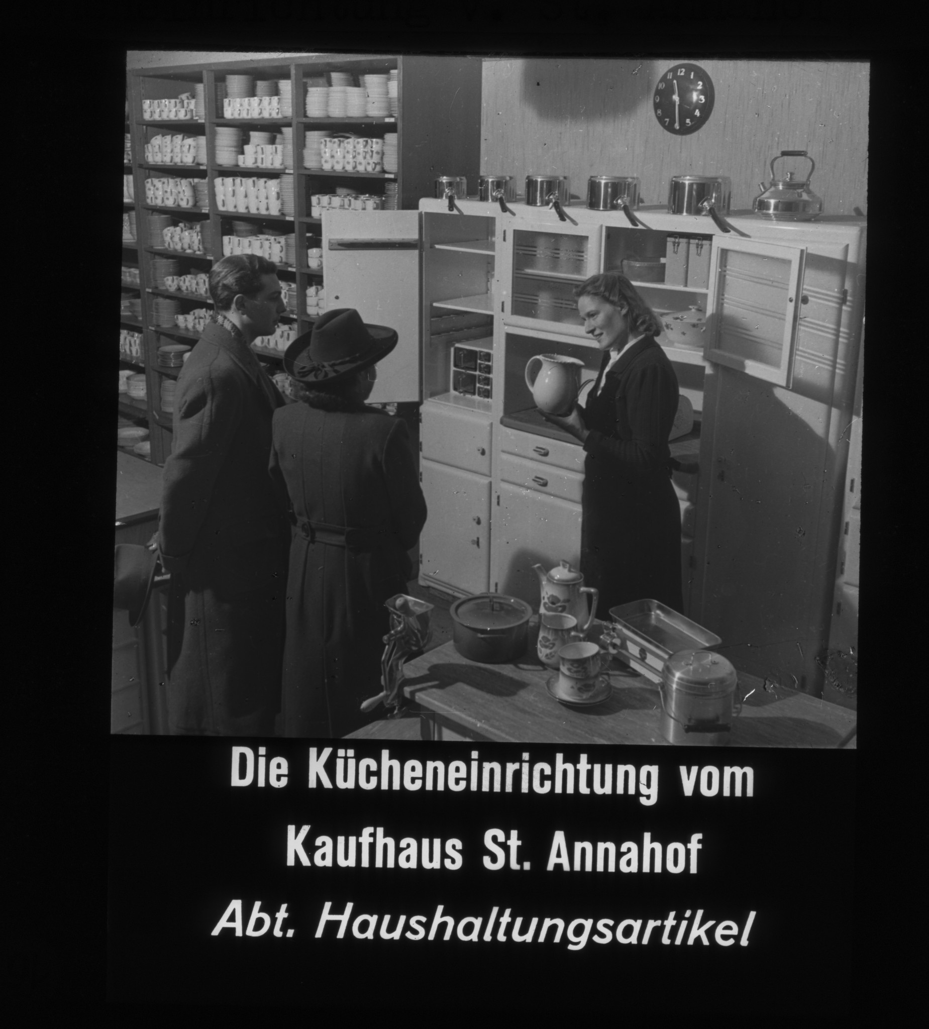 Dia: Innenansicht der Haushaltartikel-Abteilung im St. Annahof, Verkäuferin zeigt Krug, dazu Text: "Die Kücheneinrichtung vom Kaufhaus St. Annahof / Abt. Haushaltungsartikel".