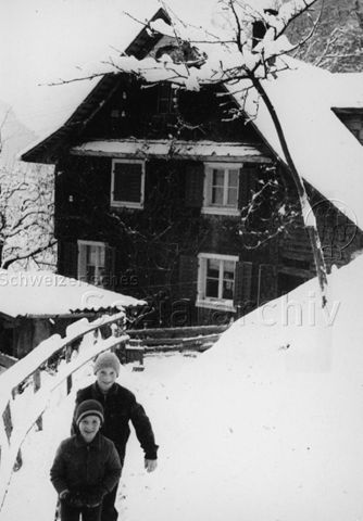 "Praktikantinnenhilfe - Die Stöckmatt, das Bergheimetli auf luftiger Höhe, Schauplatz unserer Reportage" - Zwei Kinder im Schnee vor dem Haus; um 1965