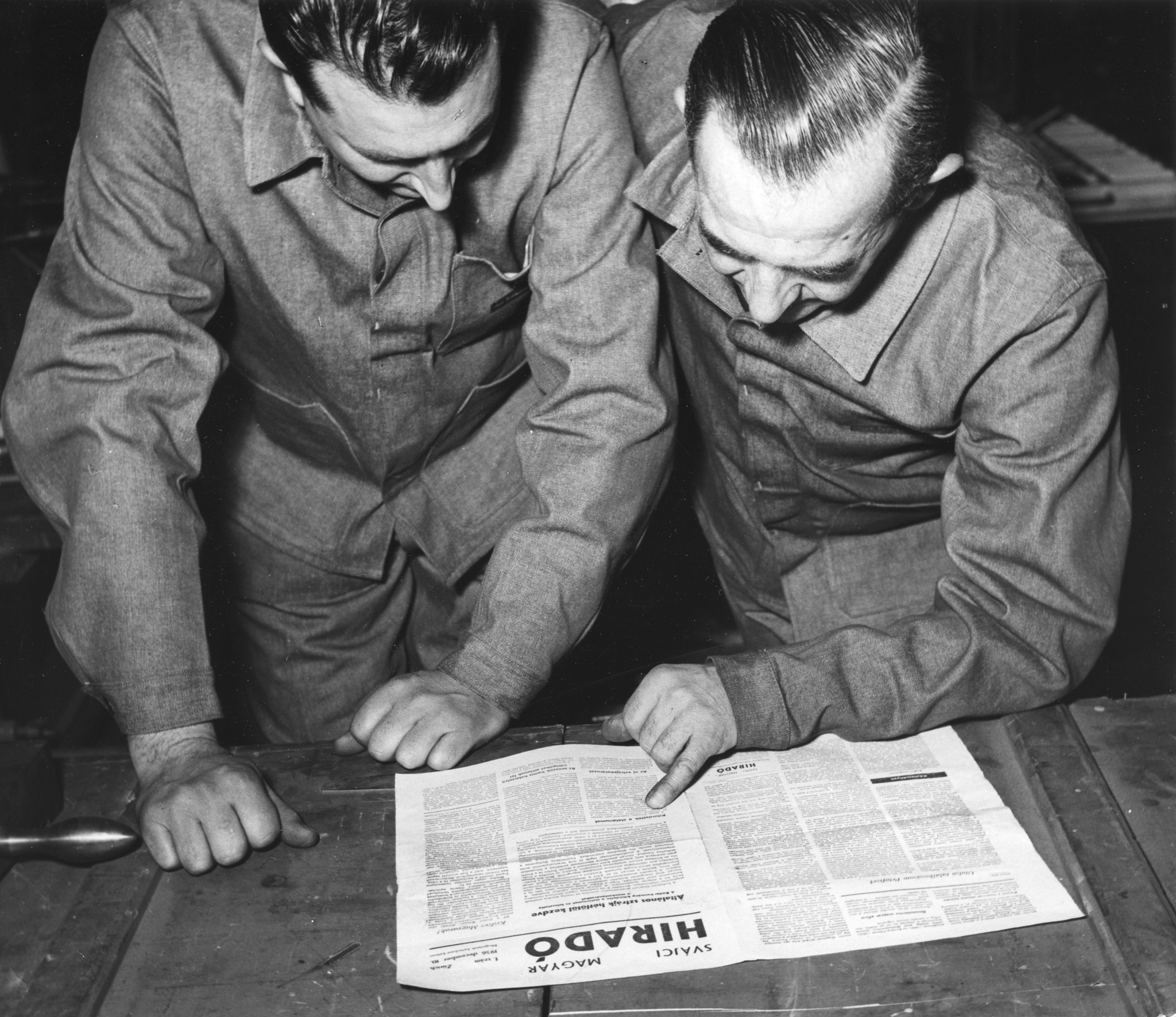 Zwei Männer in Arbeitskleidung lesen die Zeitung "Hirado"