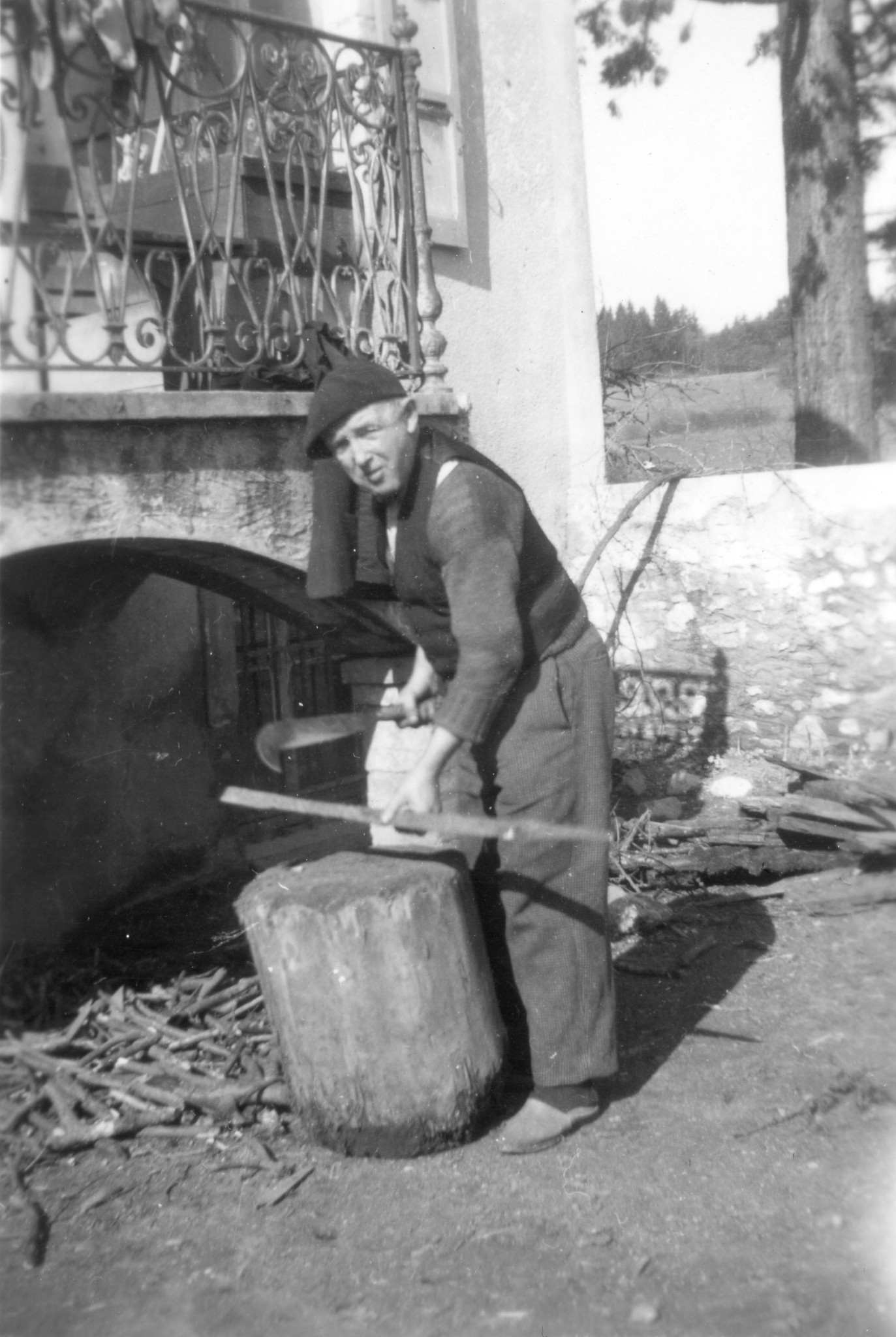 Ein Knabe bearbeitet vor dem Haus das Holz