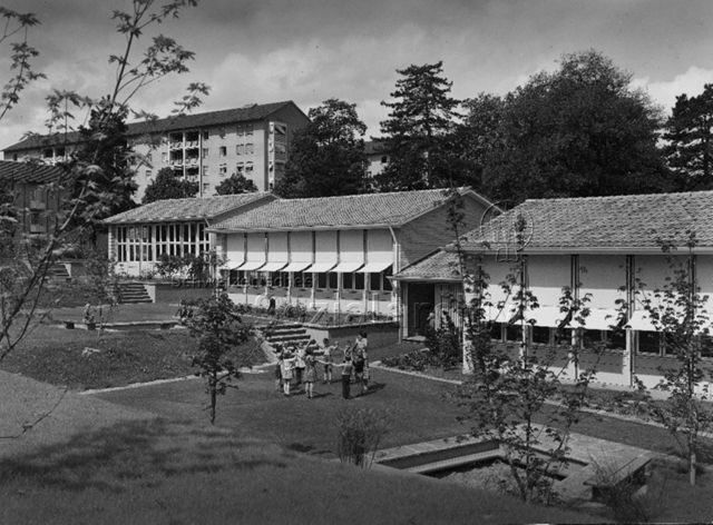 "3 Kindergärten, Burgfelderstrasse, Basel, Arch. Hochbauamt" - Kinder und Kindergärtnerin beim Spielen auf der Wiese; um 1960