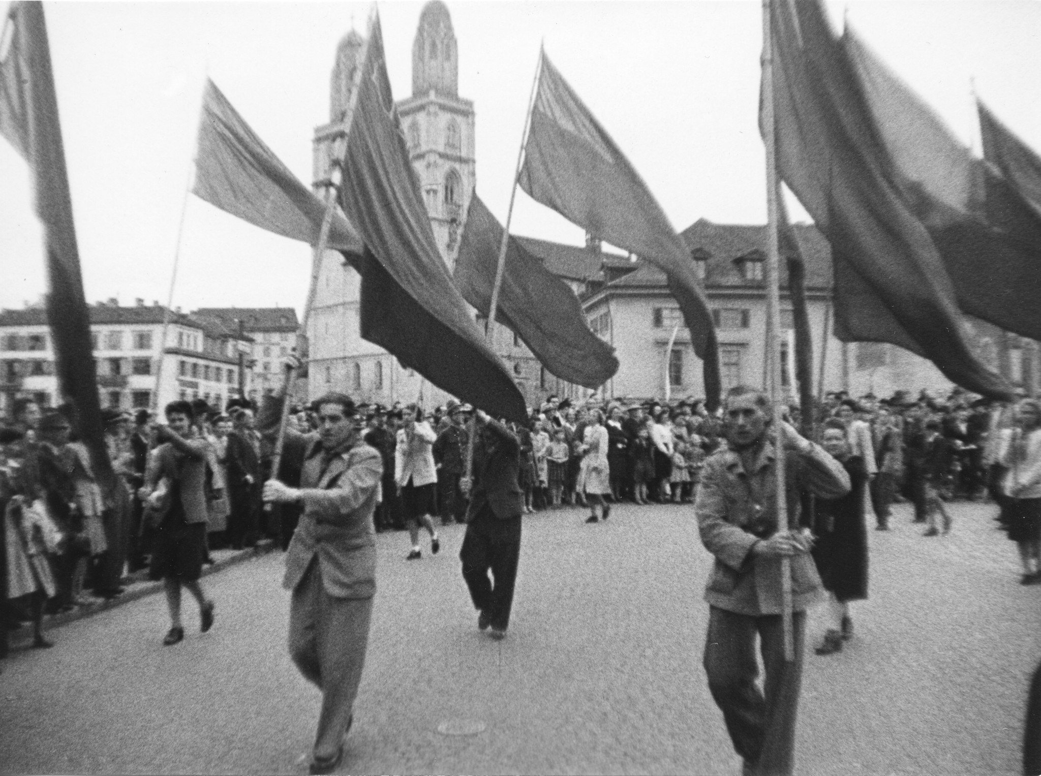 Eine Gruppe mit Fahnen marschiert durch die Altstadt von Zürich, im Hintergrund das Grossmünster