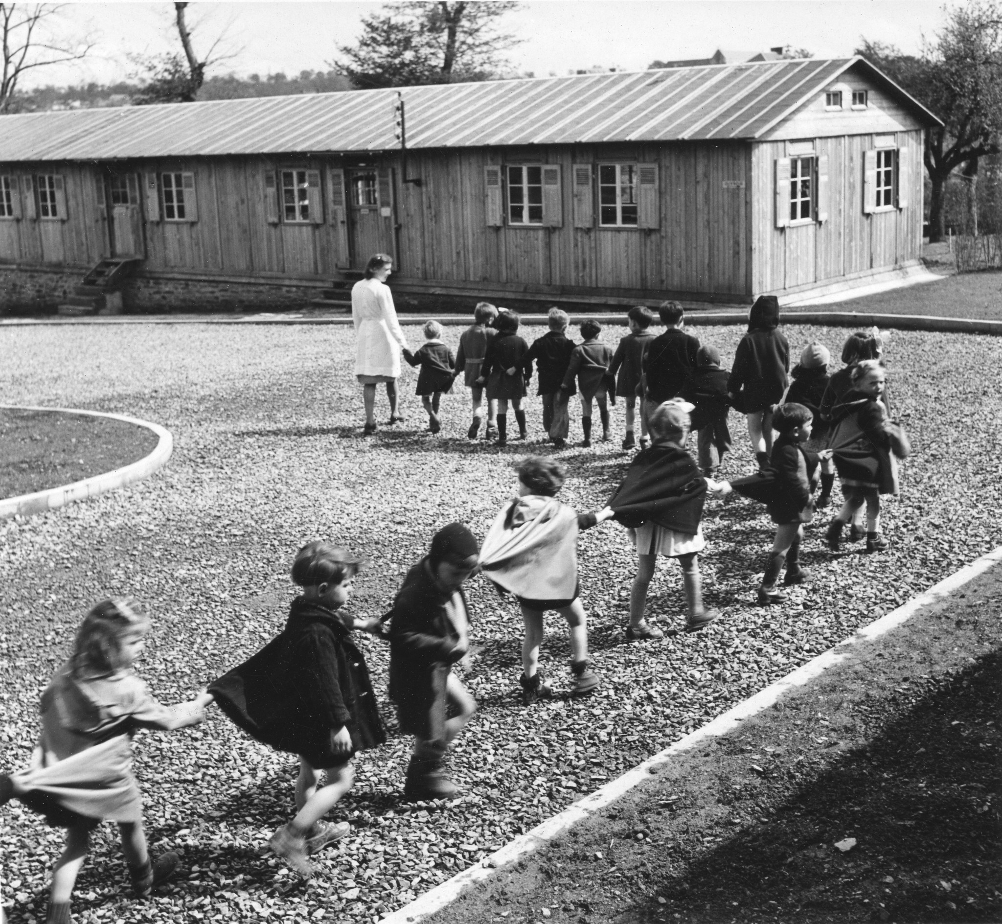 "Saint-Lô, Kindergarten", Kinderreihe mit Kindergärtnerin , vermutlich um 1946, [Sozialzentrum des SAH, "Don Suisse", "Ouvert à toute la population de St-Lô"]