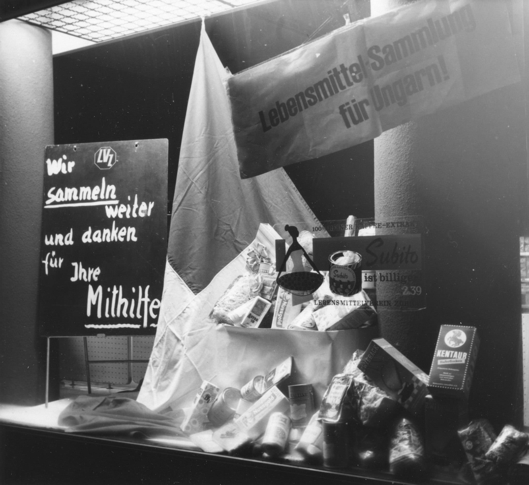 Schaufenster des Lebensmittelvereins Zürich (LVZ) mit Esswaren und Schildern mit den Aufschriften "Lebensmittelsammlung für Ungarn!" und "Wir sammeln weiter und danken für Ihre Mithilfe"