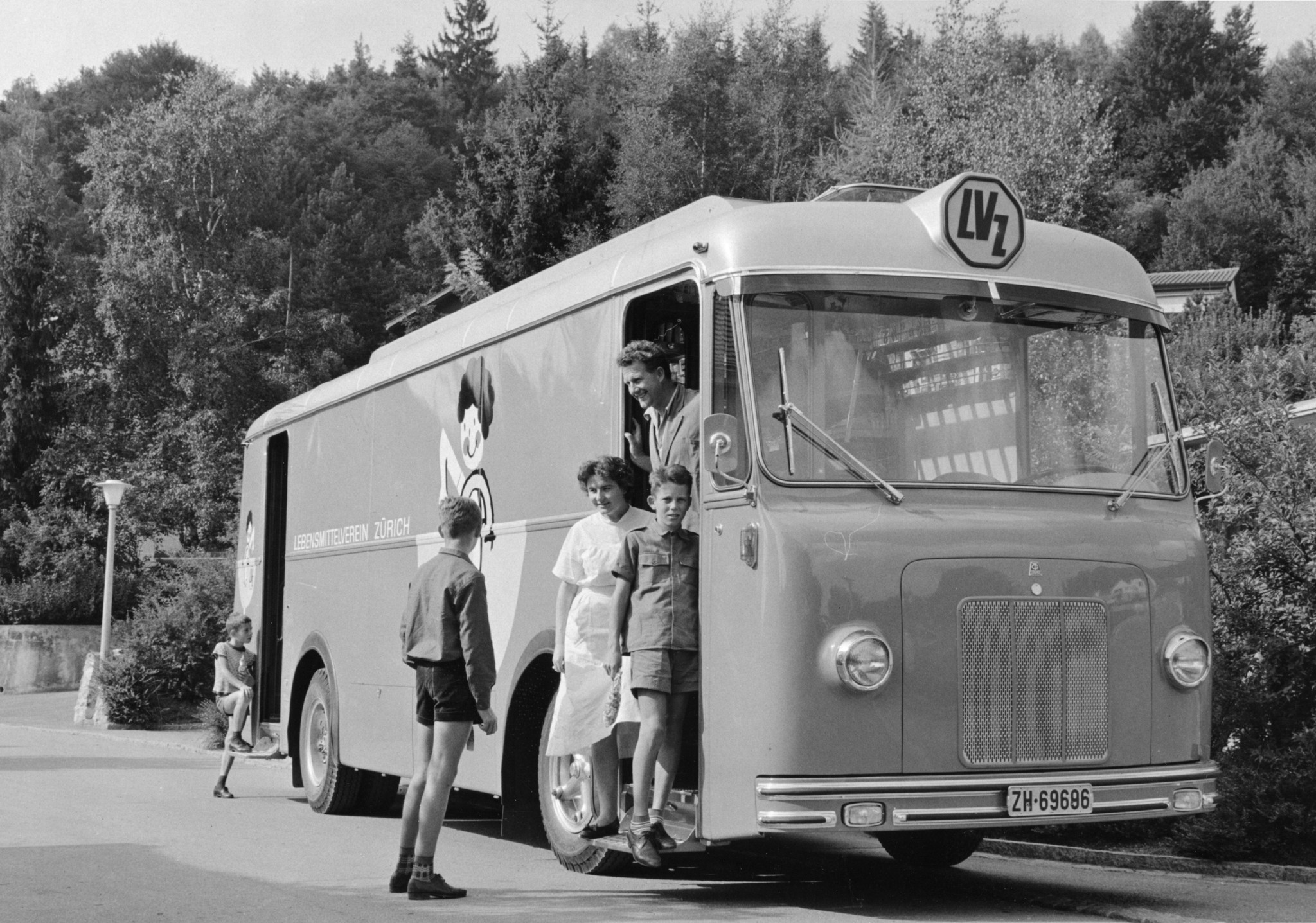 Angestellter und weitere Personen auf den Trittbrettern eines Verkaufswagen des Lebensmittelvereins Zürich