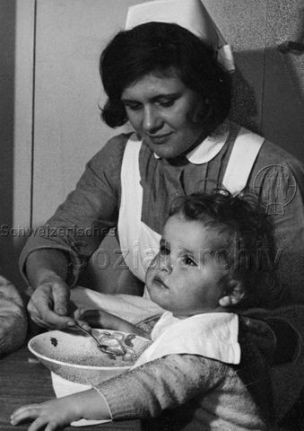 "Heimkinder, Tutti-Reportage" - Betreuerin füttert Kleinkind; um 1960