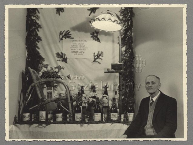 STFV-Mitglied sitzt neben vollem Gabentisch mit Schild "Einen schönen Lebensabend wünschen wir unserem treuen Mitarbeiter Robert Lüthy und Familie", 31.12.1952