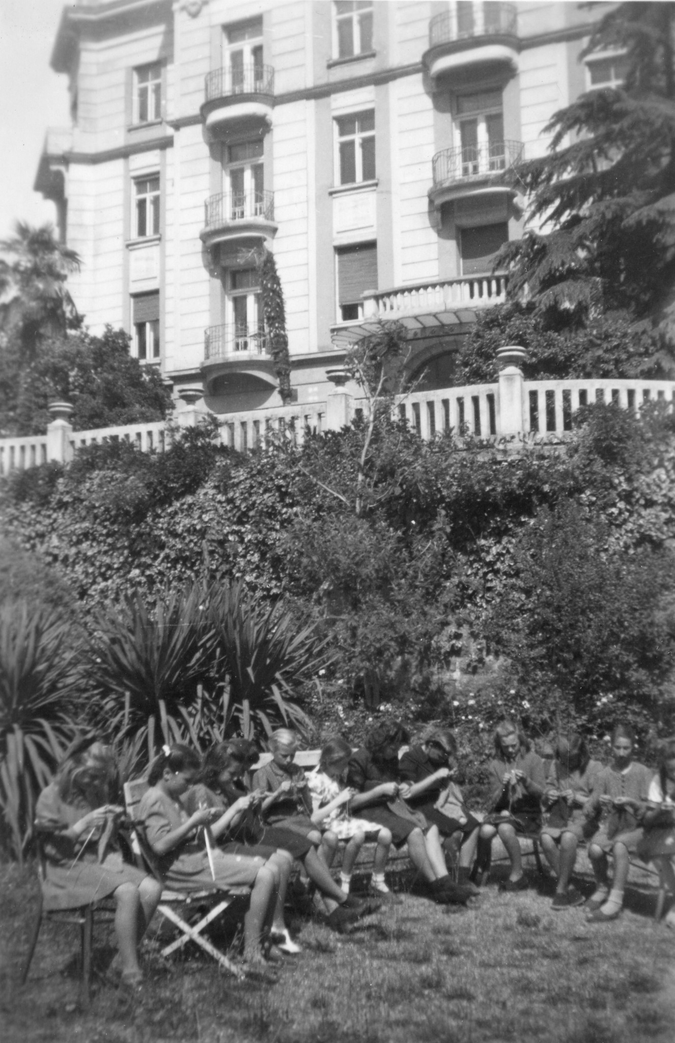 "Ein Teil der Mädchen von der Arbeitsstunde. Wir arbeiten meistens im Garten."; Mädchen sitzen im Garten und stricken