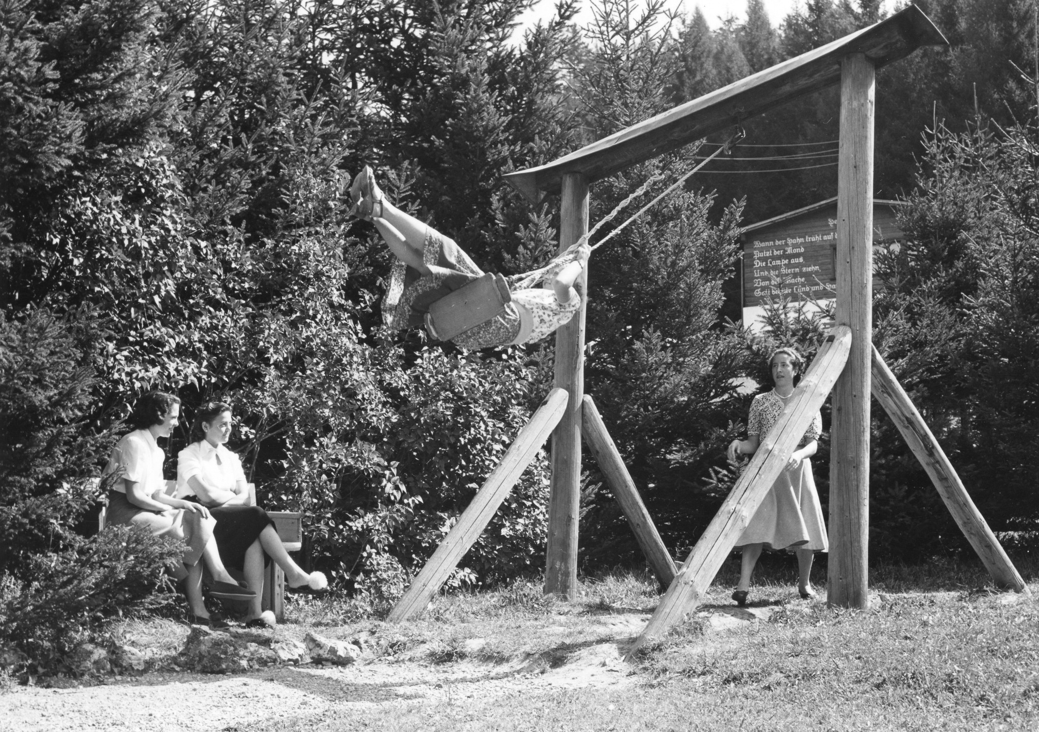 Jugendliche auf dem Spielplatz, ein Mädchen sitzt auf der Schaukel