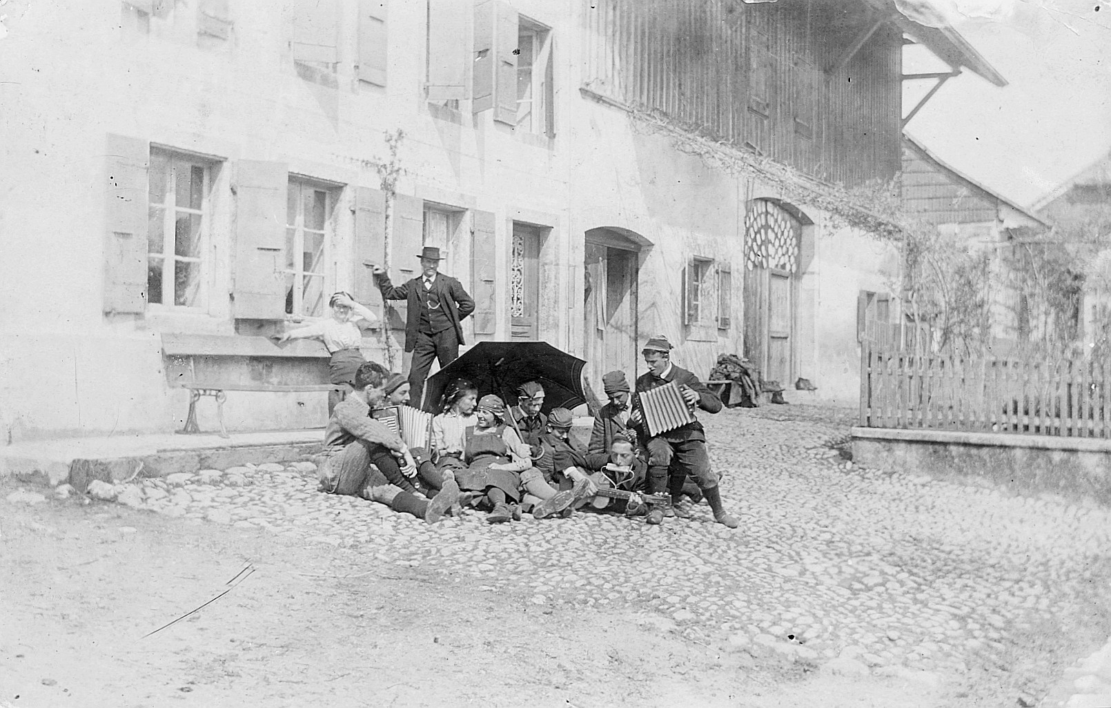 Jura-Wanderung: Wandervögel sitzen vor einem Haus auf dem Steinpflaster - Einige spielen Gitarre, Mundharmonika und Akkordeon (1913)