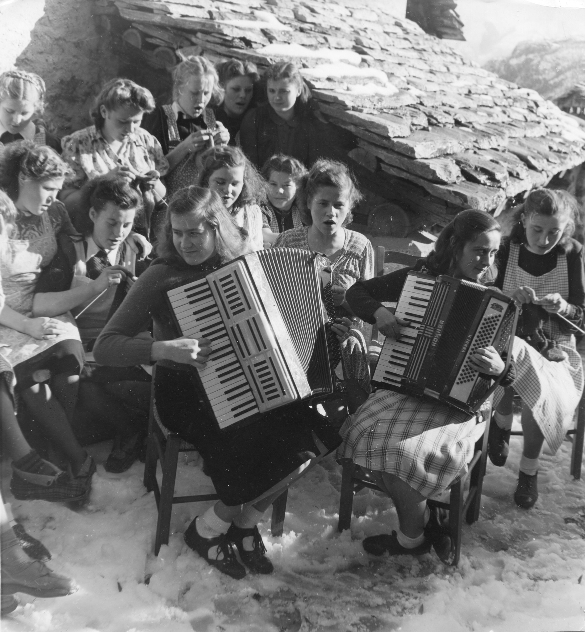 Mädchen sitzen auf Stühlen im Schnee und musizieren und stricken