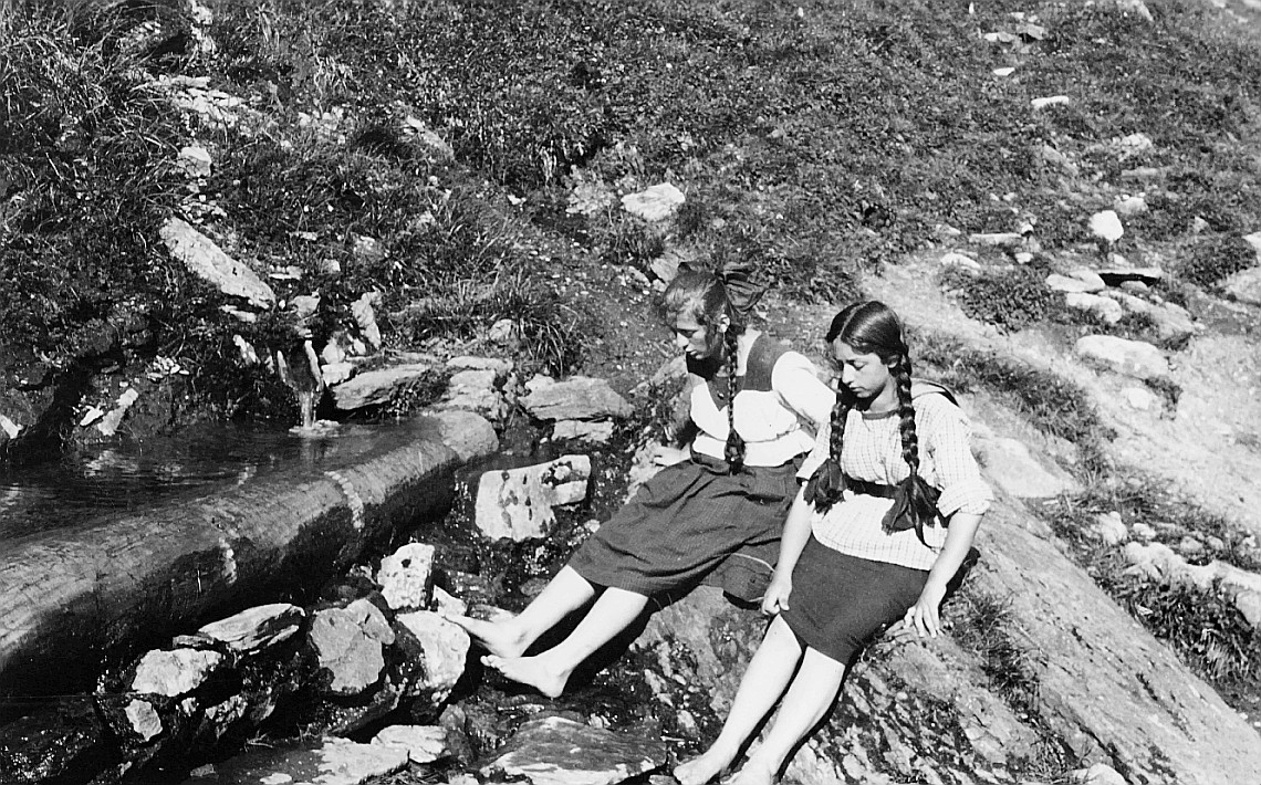 Grosse Sommerfahrt nach Engelberg/Engstlensee: Zwei Mädchen sitzen auf einem Stein und legen ihre Füsse in einen Bach - Mädchen der