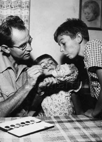 "Malen" - Vater und zwei Kinder bemalen mit Wasserfarben einen Stein; um 1970