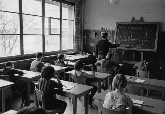 "Schule", Mathematikunterricht - Lehrer steht an der Tafel, Kinder hören aufmerksam zu; um 1970