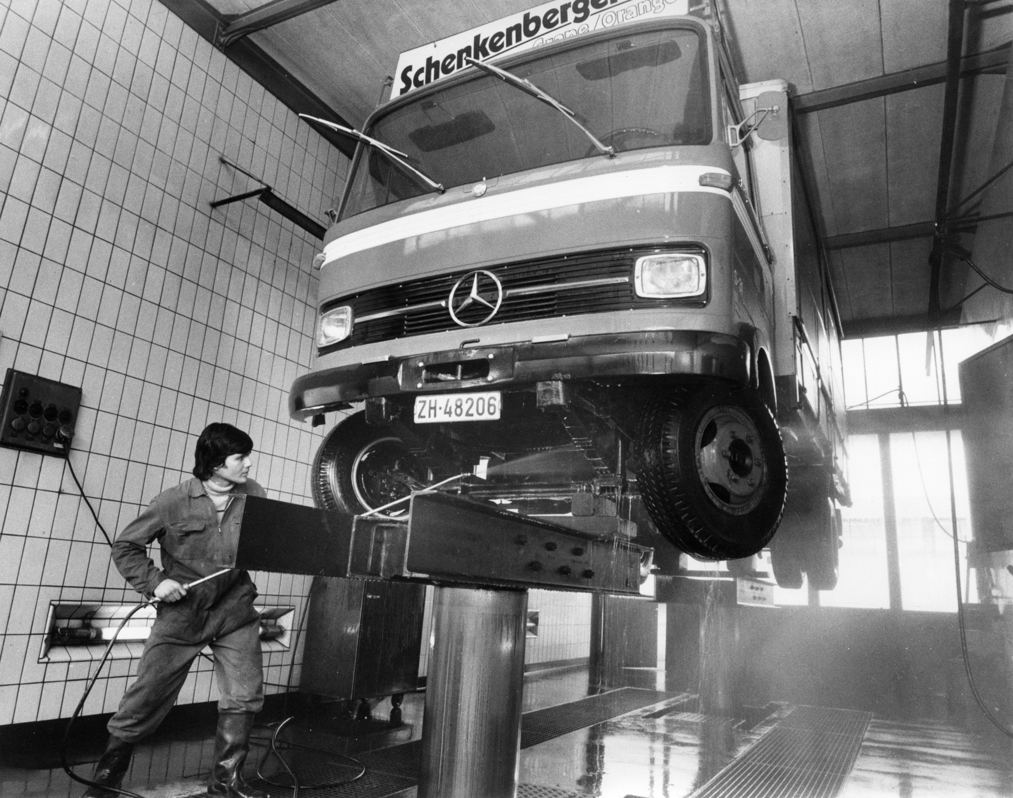 Mann beim Reinigen des Unterbodens eines aufgebockten Lastwagens mit einem Hochdruckreiniger