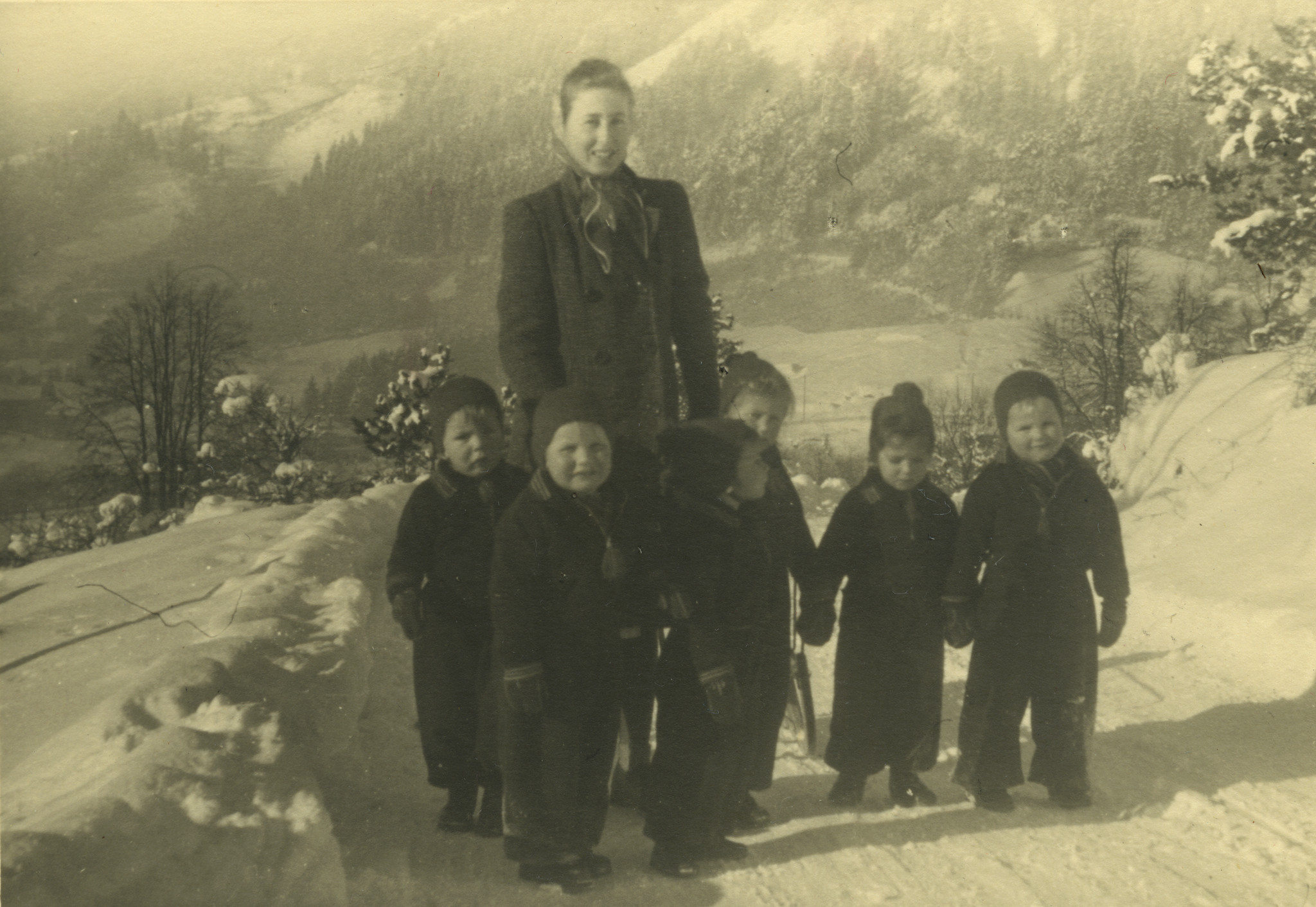Eine Frau mit sechs Kleinkindern im Schnee spazierend, vermutlich eine Kinderbetreuerin mit Heimkindern