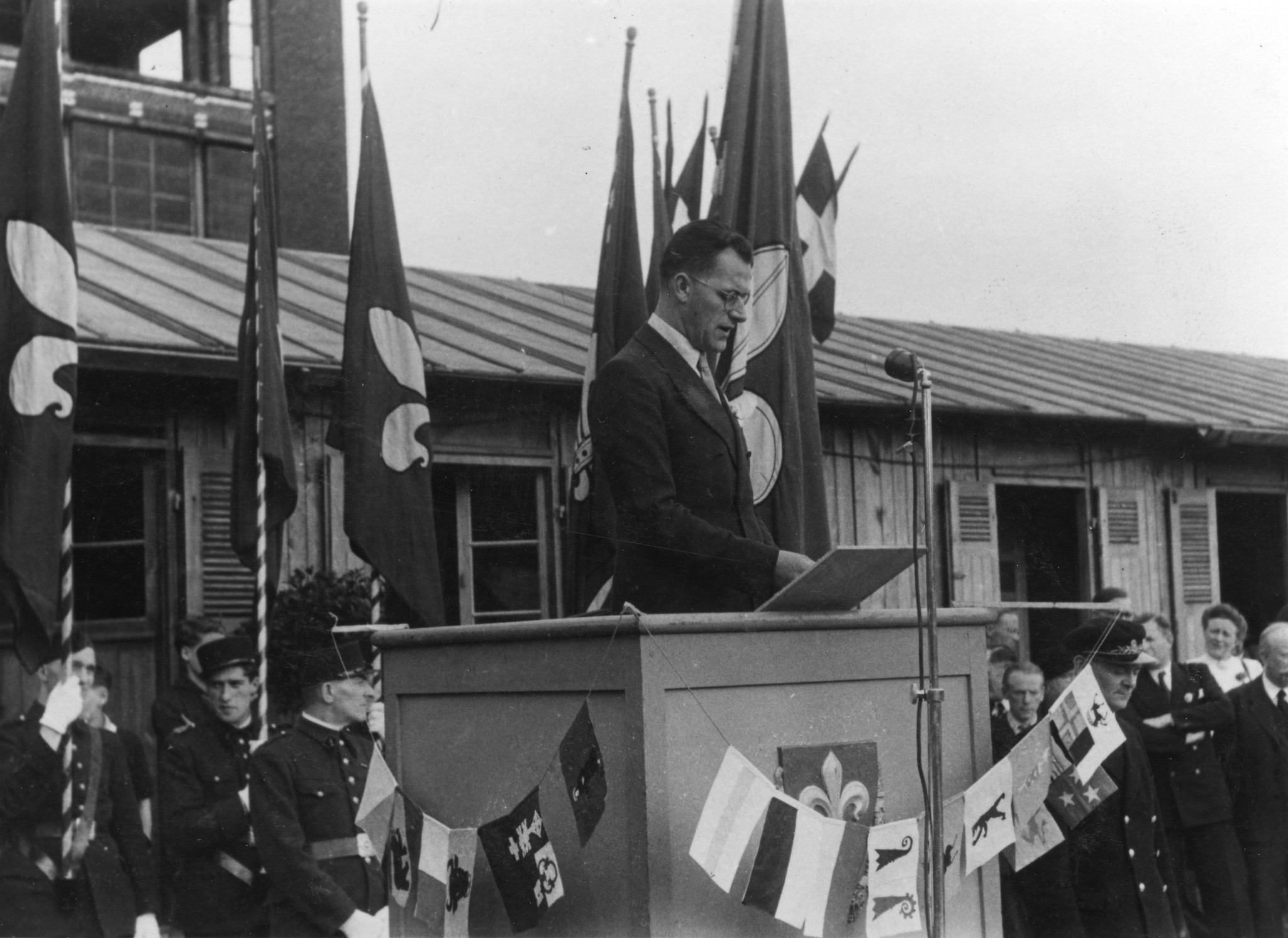 "Eröffnungsfeier des Centre social am 11. Mai 1947"; ein Mann hält eine Ansprache, im Hintergrund die Fahnen mit der Lilie