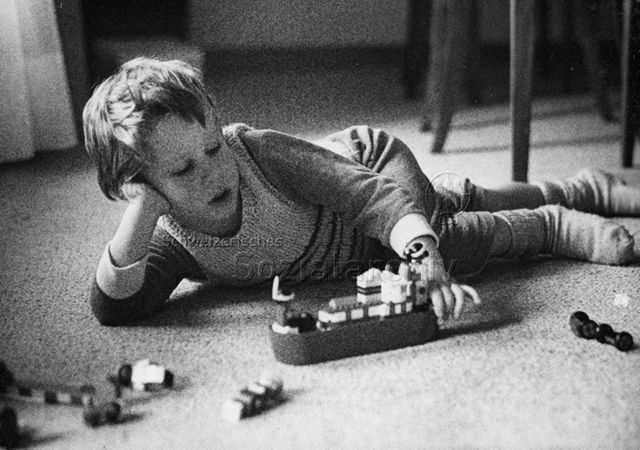 "Freizeitbeschäftigung innen" - Junge liegt auf dem Fussboden und spielt mit einem Lego-Schiff; um 1965