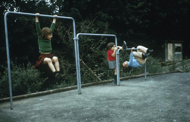 "Siedlungs- und Quartierspielplätze: Turnstangen Siedlungsspielplatz Adliswil ZH" - Drei Kinder spielen an verschieden hohen Turnstangen im Freien; um 1970