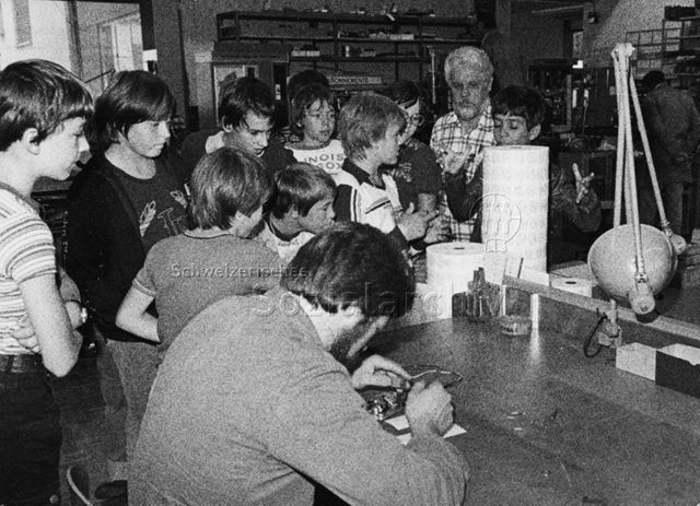 "Ferienpass" - Kinder in der Werkstatt, vorne sitzt ein Mann bei Elektronikarbeiten; 1979