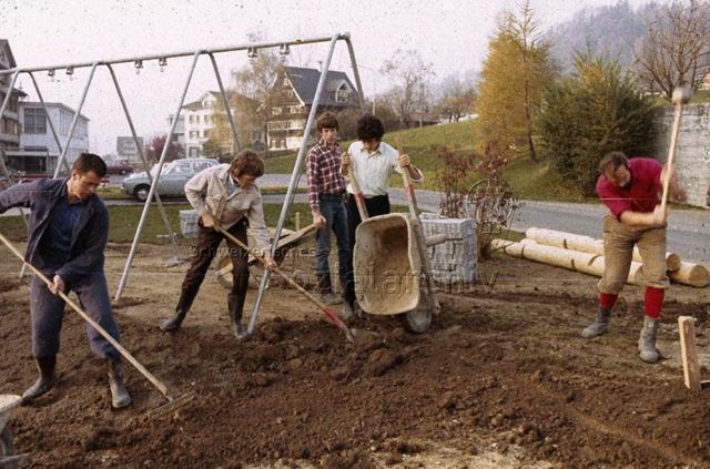 "Siedlungs- und Quartierspielplätze: Siedlungsspielplatz Stocken, Ebnat-Kappel SG" - Baustelle des Kinderspielplatzes auf einer grossen Wiese, junge Leute ebnen den Boden; um 1970