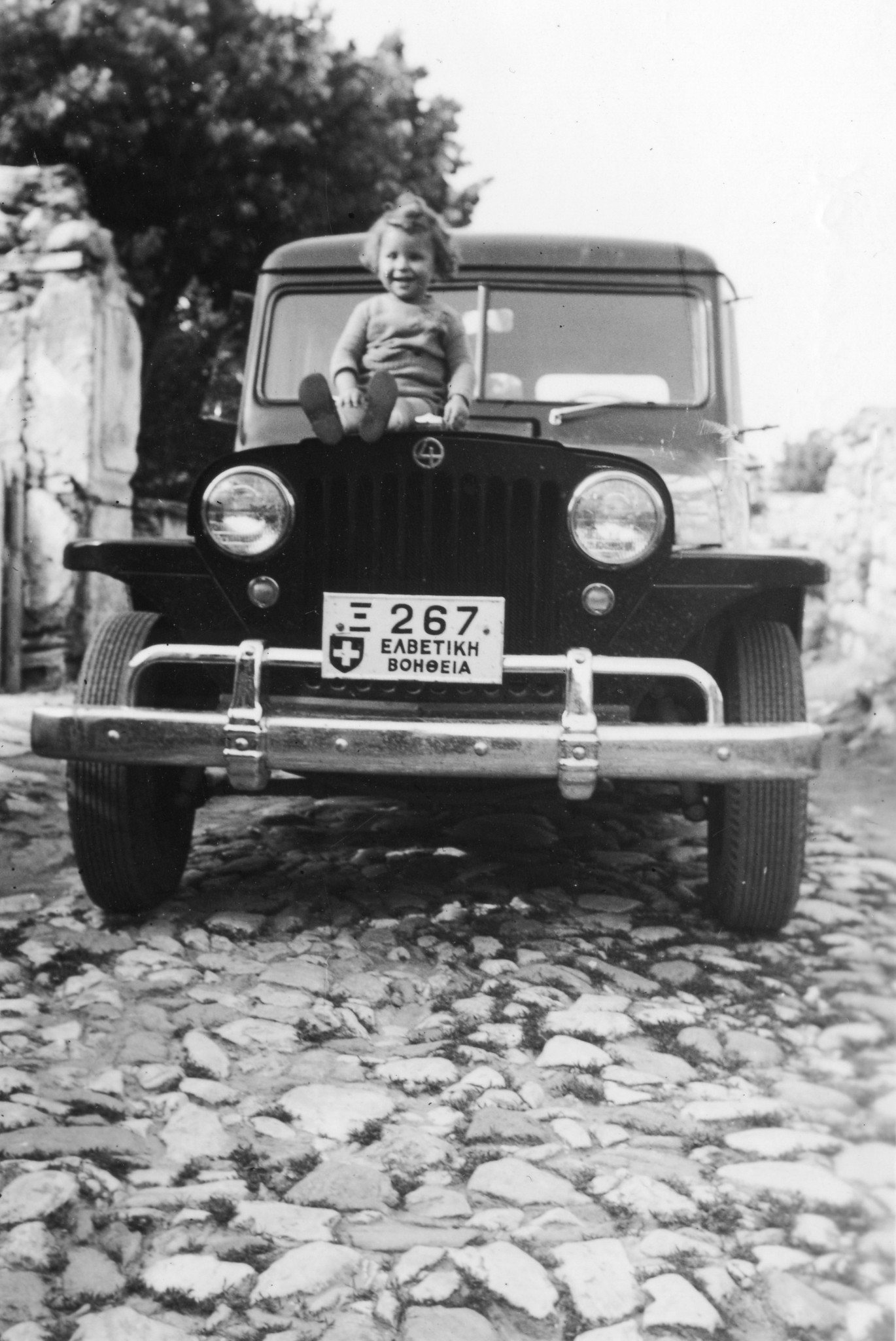 "Nikos, unser Freund in Sevoia". Ein Kleinkind auf der Kühlhaube eines Wagens sitzend