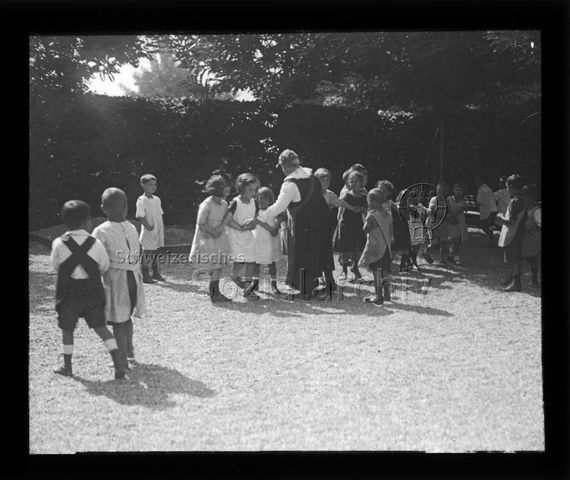 Diaserie zum Thema Kindergarten / Schulkind; Kinder und eine Frau tanzen auf einem Kiesplatz; um 1930