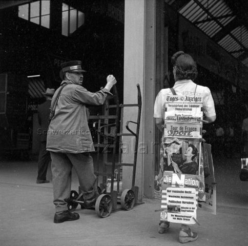 Gepäckträger, Frau mit Reklame-Sandwich (diverse Zeitungsaushänge), Zürich Hauptbahnhof, um 1960