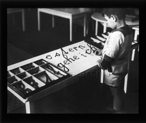 Diaserie zum Thema Kindergarten / Schulkind; ein Junge am Auflegen von vorgefertigten Schulschrift-Buchstaben "Ostern gehe ich"; um 1930