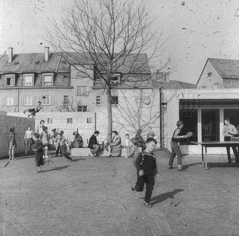 "Freizeitanlagen, Gemeinschaftszentren: Hartplatz FZA Buchegg, Zürich" - Kinder beim Spielen in einem gepflasterten Innenhof; um 1965
